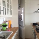 weiße Küche perspektivisch dargestellt (links und rechts). Am Ende des Bildes ist der halb geöffnete Kühlschrank ersichtlich.
