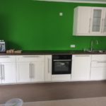 Küchenzeile mit weißen Holzfronten, Arbeitsplatte in dunkler Nuss und moosgrüne Wandfarbe
