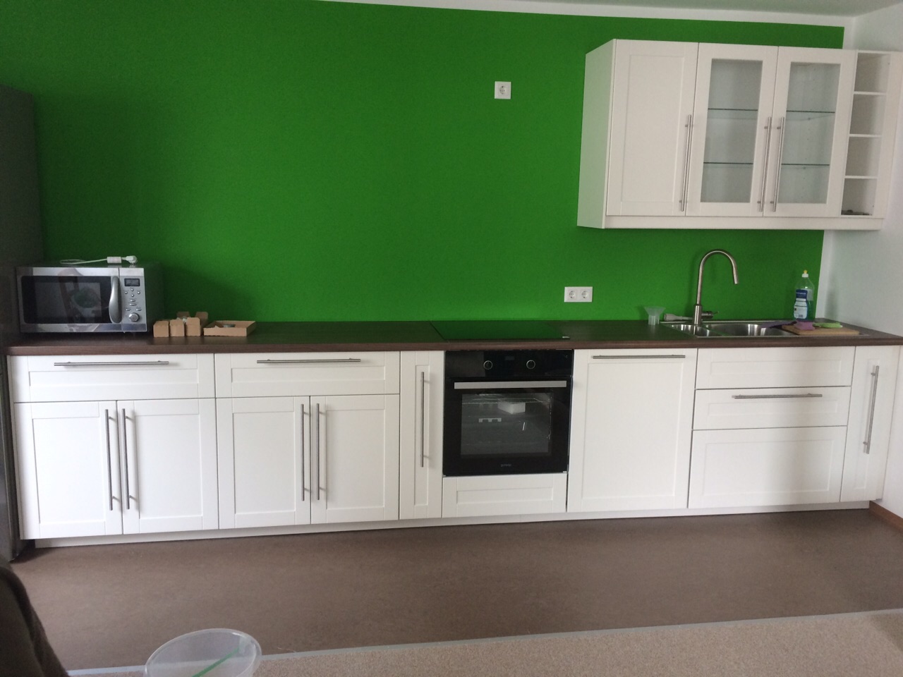 Küchenzeile mit weißen Holzfronten, Arbeitsplatte in dunkler Nuss und moosgrüne Wandfarbe