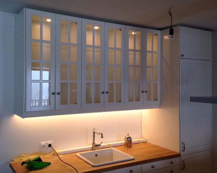 Diese weiße Küche im Landhausstil ist mit ihren beleuchteten Glasfronten an den Oberschränken ein richtiger Blickfang! Das Porzellanwaschbecken sowie die Vollholzarbeitsplatte geben ihr den nötigen Schliff.