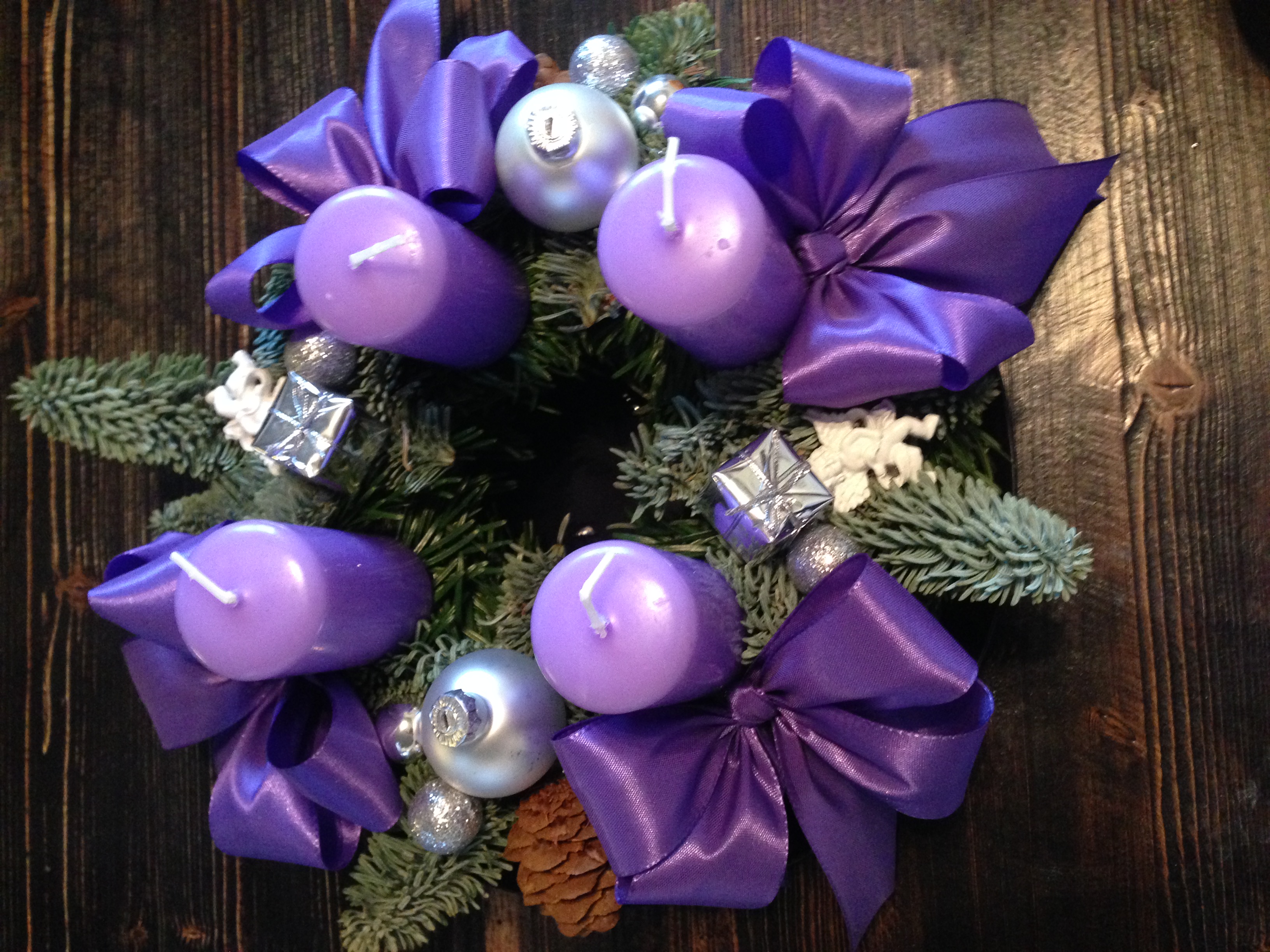 Adventkranz mit violetten Kerzen, silbernen Weihnachtskugeln und purpurnen Stoffmaschen